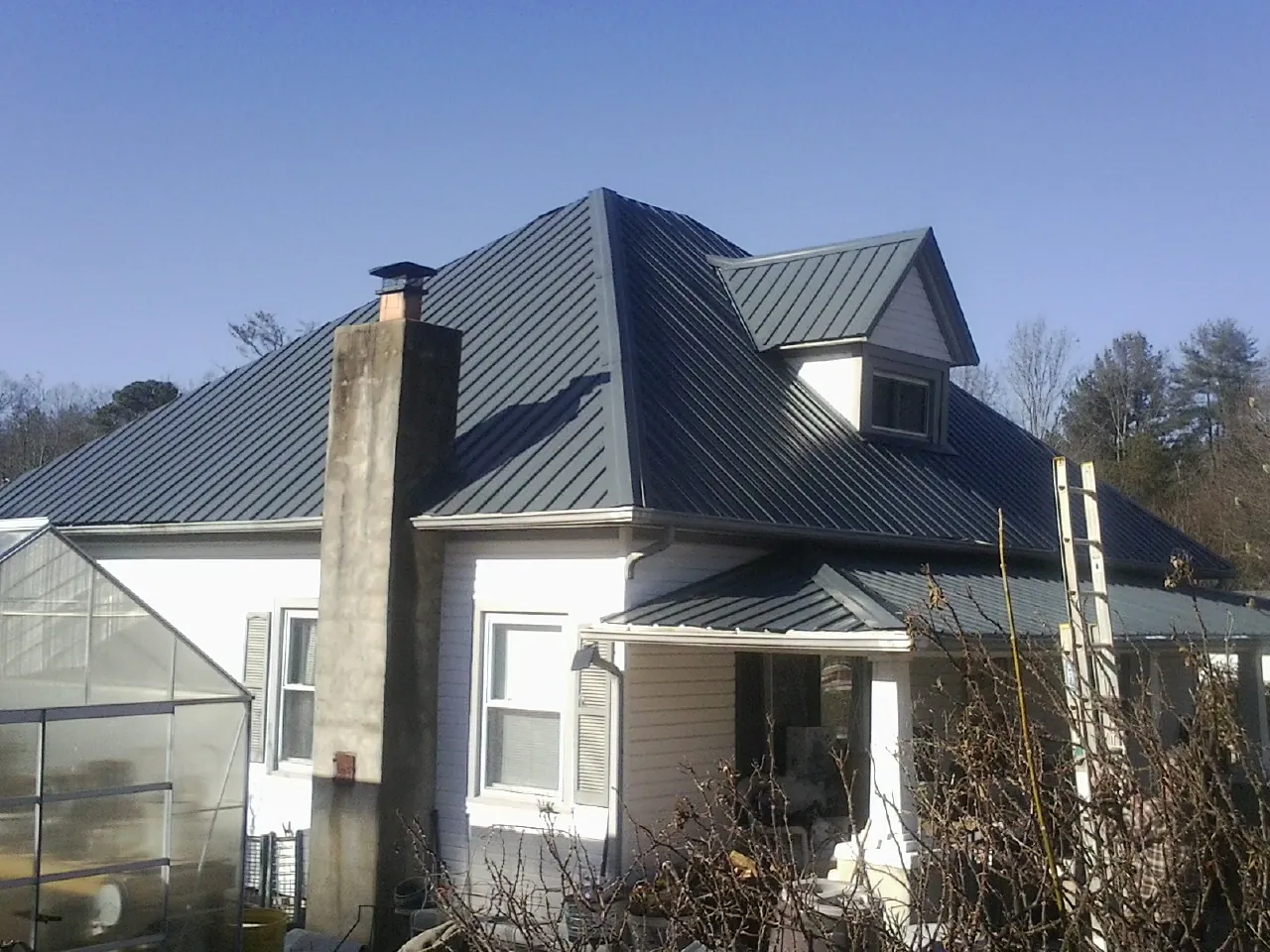 Dark blue standing seam metal roof on a white farmhouse with dormer — Slate & Tile Roof Repair by Roofing Brothers in Cassandra