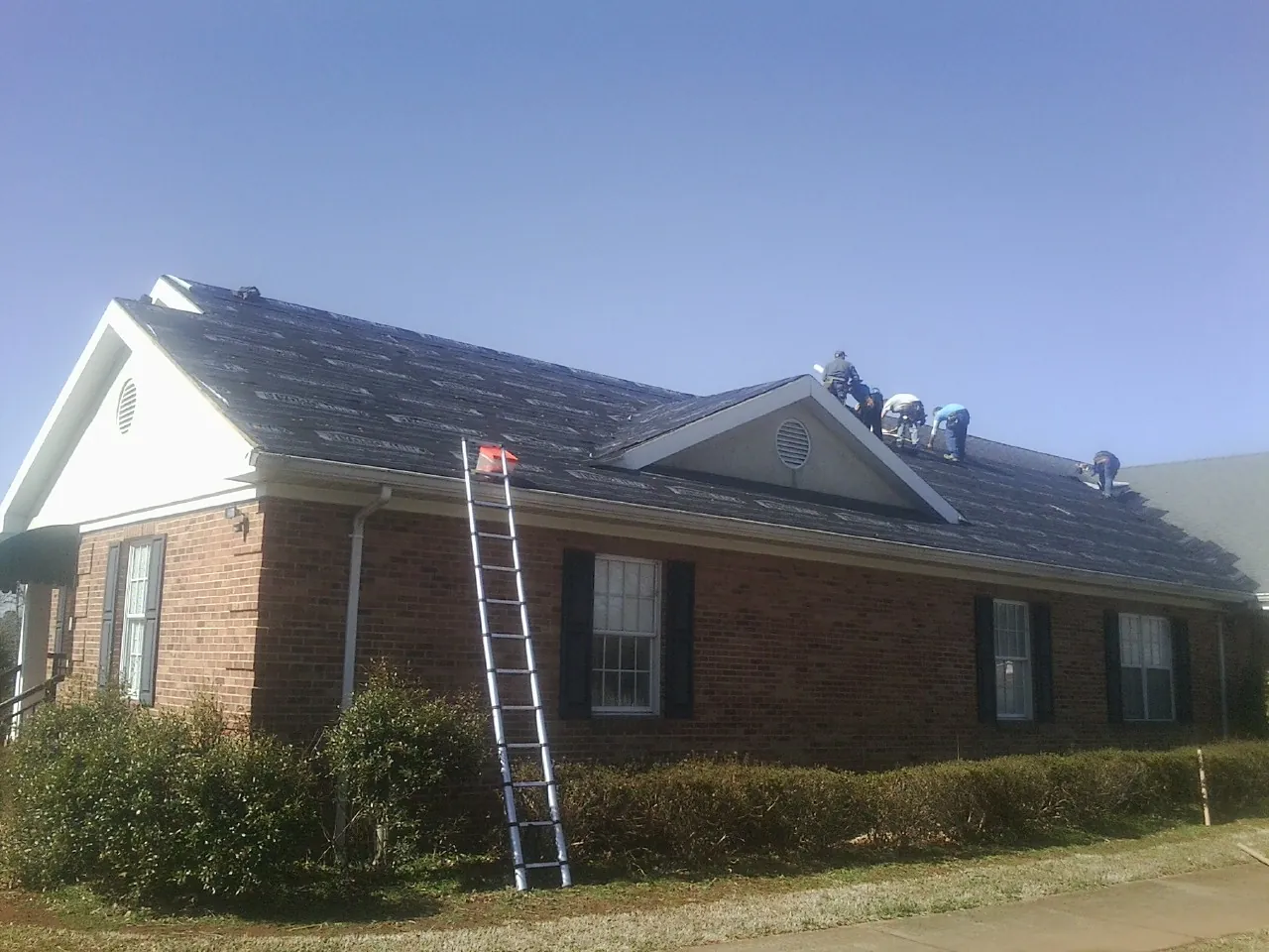 Crew tearing shingles off a brick ranch roof with a ladder set — Emergency Roof Repair work by our crew in Cassandra