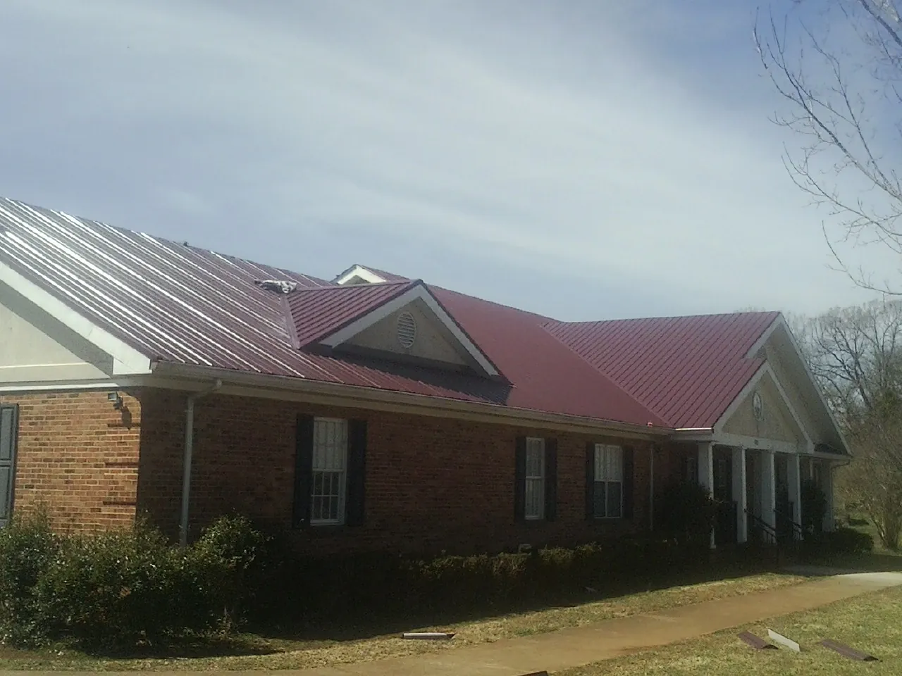 Red metal roof with gabled entries on a long brick building, from a Hail Damage Roof Repair job in Cassandra