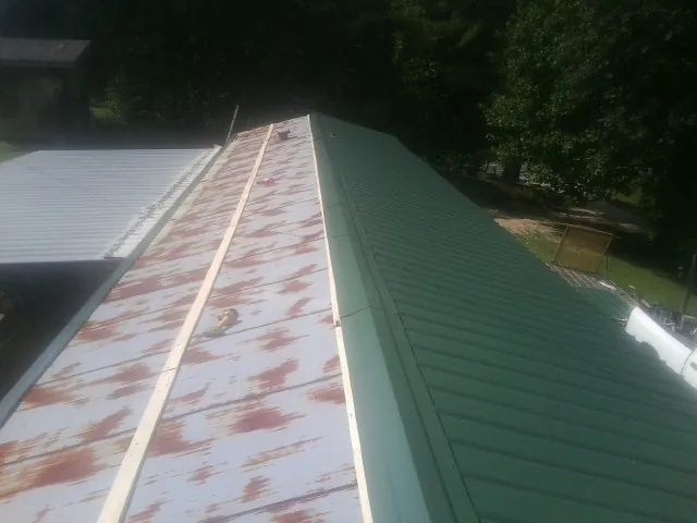 Old rusted panels beside newly installed green metal roofing — Wind Damage Roof Repair by Roofing Brothers in Cassandra