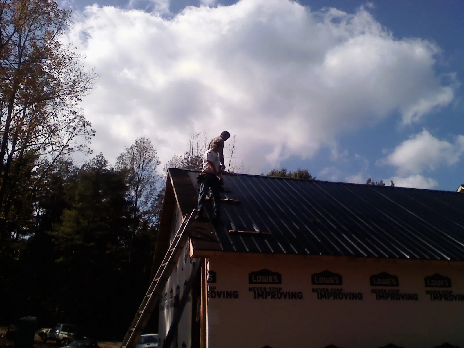 Roofer fastening dark metal panels high against a cloudy sky, from a Roof Inspection job in Cassandra