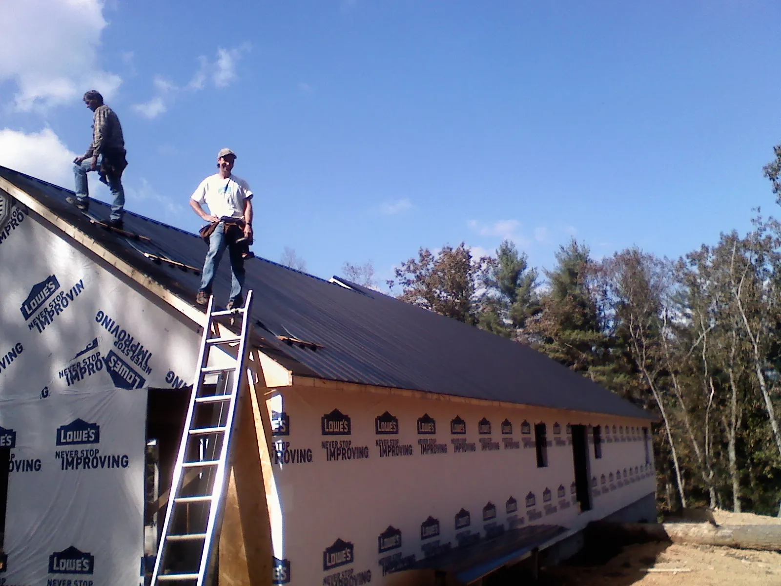 Two roofers standing on a long dark metal roof over a wrapped building in Cassandra