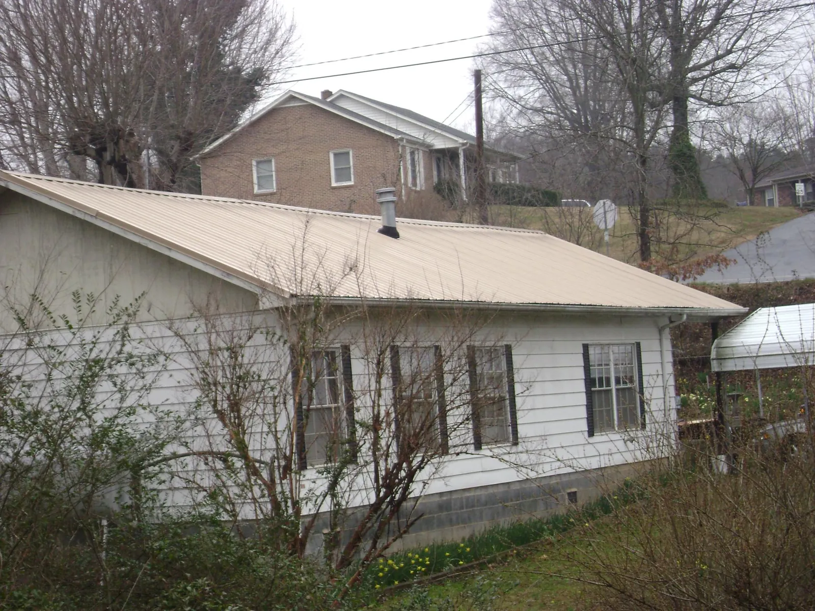 Tan metal roof on a white sided house set into a hillside — Commercial Roofing by Roofing Brothers in Cassandra