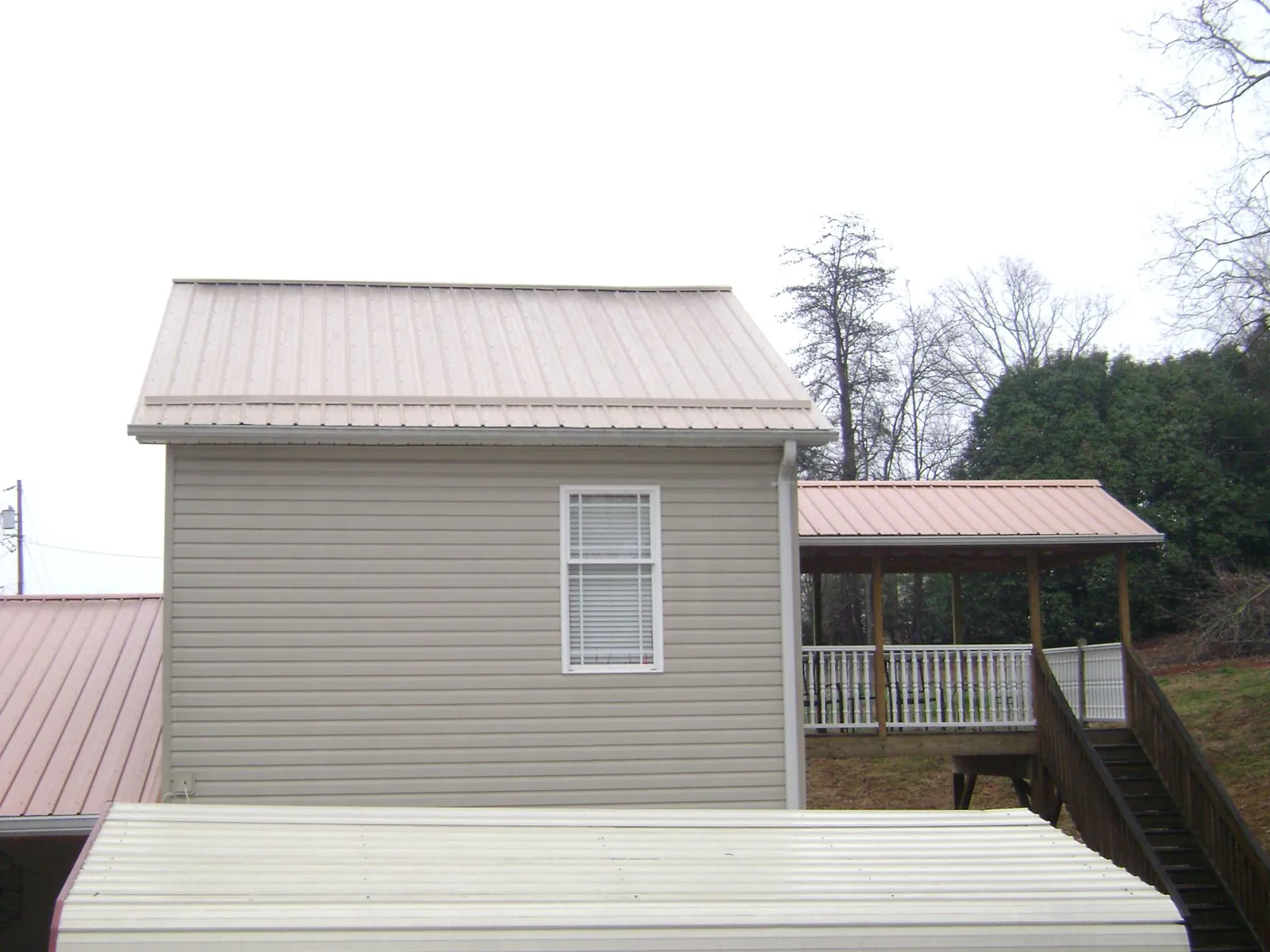 Tan metal roofs on a two story addition and attached porch, from a Roof Replacement job in Cassandra